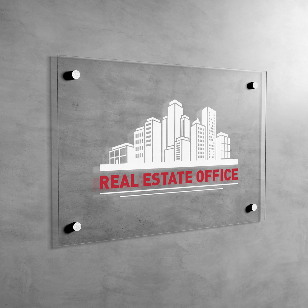 Glass sign with cityscape design and 'Real Estate Office' text on a concrete wall.
