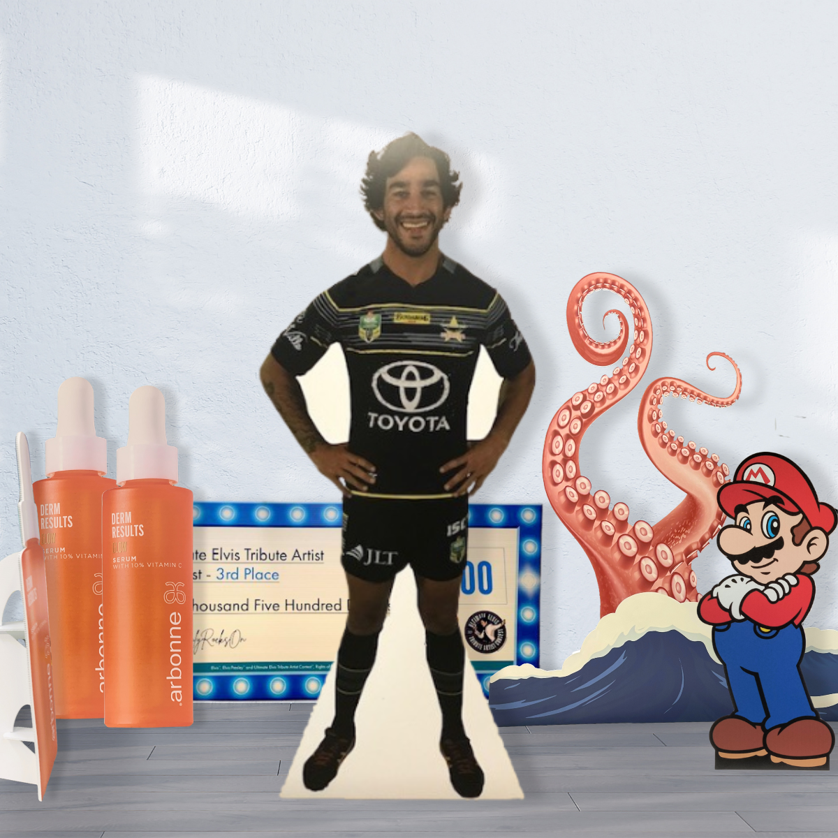 A People Cutouts | Standees | Cut to Shape Display of a rugby player stands in a room with Arbonne skincare bottles, shaped corflute signs, a giant check, a tentacle, and a Mario character illustration scattered nearby.