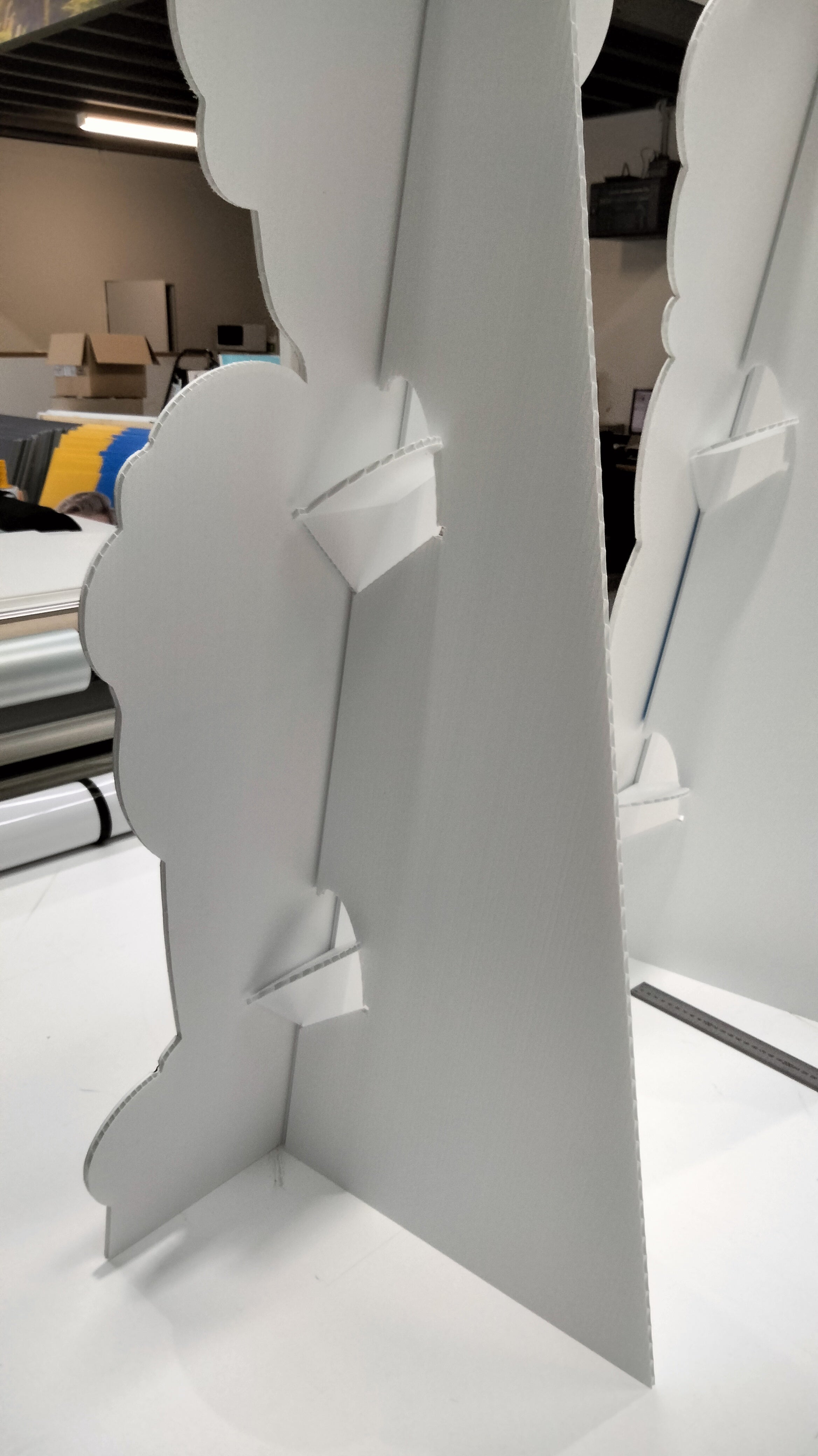 A close-up of a white People Cutouts | Standees | Cut to Shape Display with cloud-like edges, featuring interlocking support pieces holding the cutout upright on a table in a workspace.